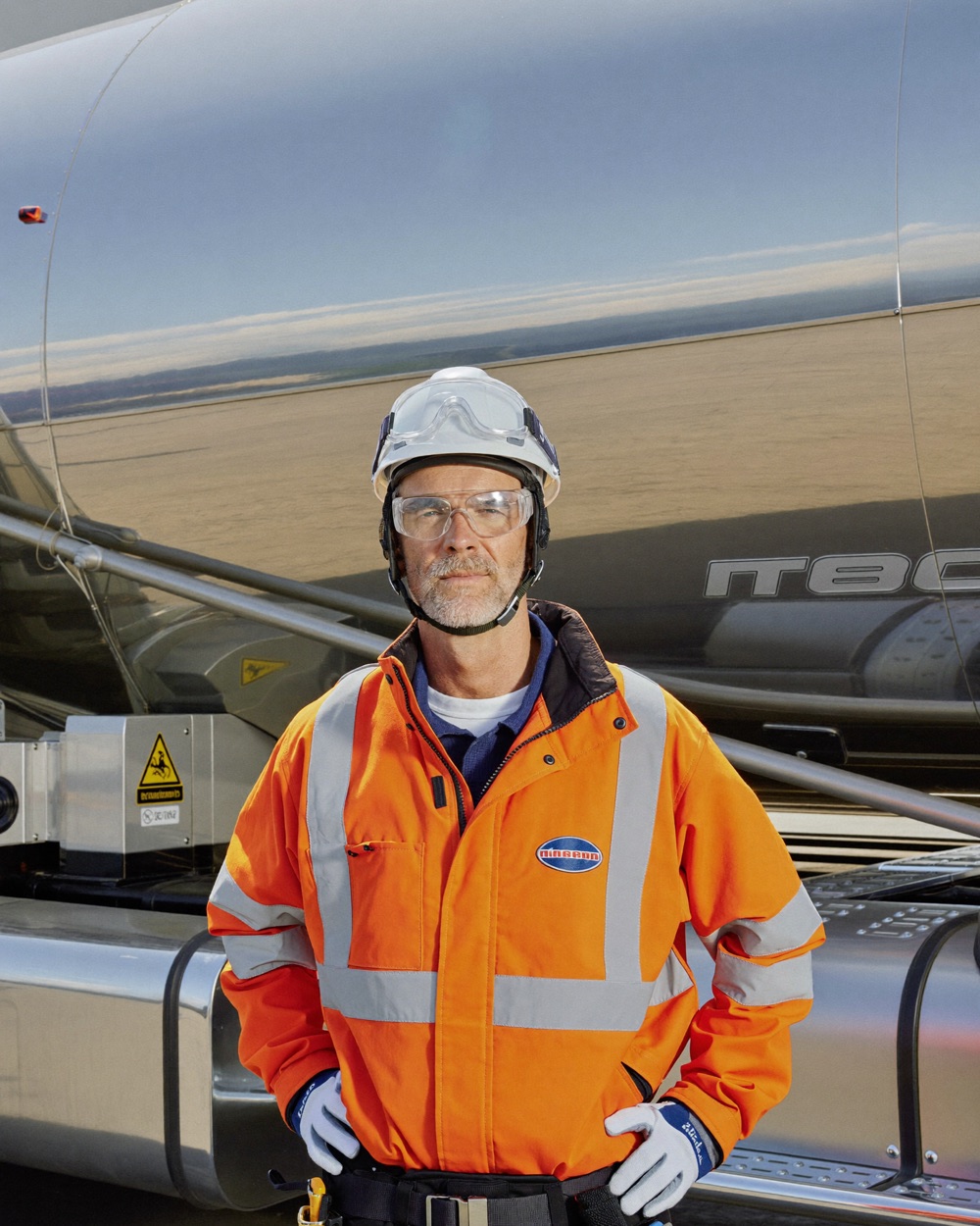 Anzeigenmotiv für Gefahrgutfahrer: Tankwagenfahrer mit Helm und Schutzbrille vor einem Edelstahl-Tankauflieger
